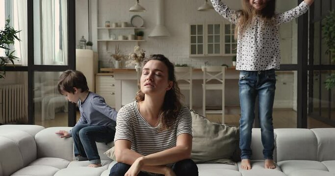 Tired single divorced woman feels annoyed and exhausted due nosy little daughter and son jumping on couch. Chronic fatigue, restless, hyperactive, disobedient kids, difficulties of upbringing concept