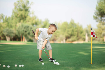 little Boy playing golf and hitting ball by putter on green grass
