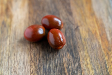 three black kumato cherry tomatoes on a wooden background vertically