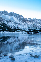 Sunny morning in Dolina Pięciu Stawów, Tatra Mountains, Poland. The valley is in the shadows, the lake is starting to freeze. Winter is coming. Selective focus on the rocks, blurred background.
