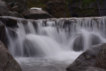 Fototapeta premium A stunning jungle waterfall flows into a cool mountain river with big rocks.