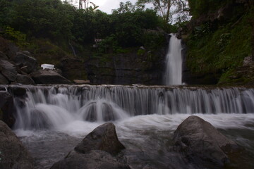 Fototapeta na wymiar A stunning jungle waterfall flows into a cool mountain river with big rocks.
