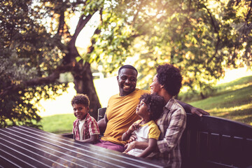 African American family sitting on bench in park.