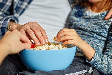 Close up of hands Mother, father and daughter eat popcorn