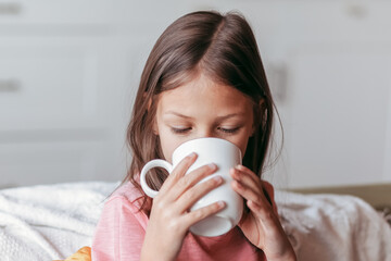 The little girl is drinking from a white mug. Close-up portrait