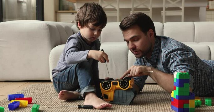 In living room father and 5s son repairing toy car play together auto mechanic hold screwdriver fixing truck have fun on floor at home. Skills transmission, share knowledge, boyhood, playtime concept