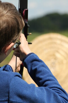 close-up of a hand holding a bow and aiming at a target, in the background a green landscape, a boy performs archery