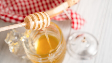 Close up wooden honey dipper. Honey flowing down a wooden spoon into a jar. Honey dipper covered by...