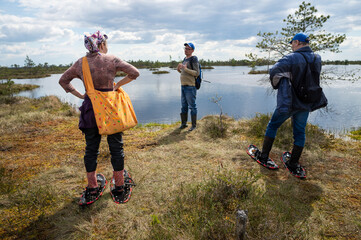 Hikers stopped by the lake. A small group of tourists travels around the reserve. People move through the swamp wearing special devices - bogshoes.
