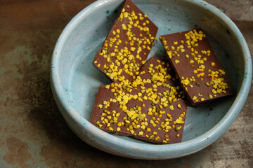 Chocolate bar with bee pollen in a blue ceramic bowl. Metal rusty surface. Rural still life. Copy space.