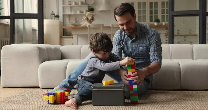 Caring dad and preschool son play colorful blocks set sit on floor in living room spend playtime together enjoy pastime and game at home. Loving father teach kid, favourite hobby and leisure concept