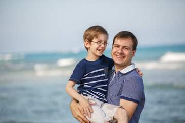 Fototapeta na wymiar Young man and boy on sea vacation. Family funny walk on a tropical beach at sunny day, enjoying summer holidays. Summer lifestyle portrait of pretty family: Dad and son. Travel in tropic country