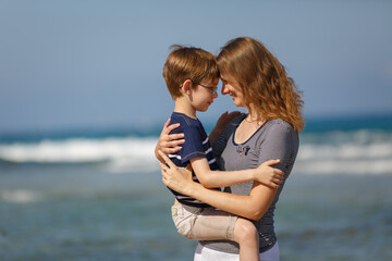 Young woman and boy on sea vacation. Family funny run on a tropical beach at sunny day, enjoying summer holidays. Summer lifestyle portrait of pretty family: mom and son. Travel in tropic country