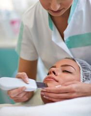 Close up of hands of beautician making cavitation treatment on human face