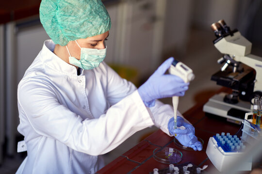 A Young Female Scientist In A Protective Gear Pipetting At The Laboratory. Science, Covid 19, Virus, Corona, Chemistry, Lab, People