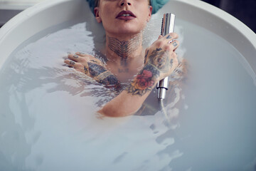 Fototapeta premium A young beautiful tattooed girl enjoying a water while having a warm bath in the bathroom. Relaxation, bath, bathroom, home