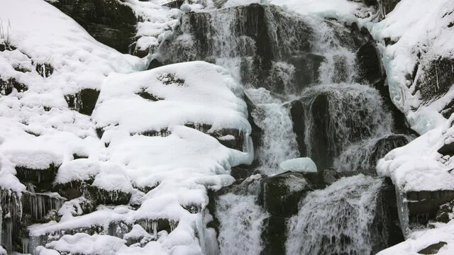 Small mountain streams of icy water flow among wet stones covered with white snow, 3x slow-mo