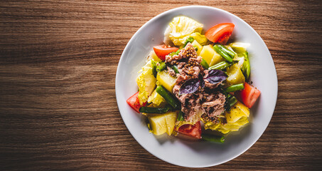 Salad nicoise. Tuna, with green beans, tomatoes, potatoes and a vinaigrette mustard dressing in white plate on wooden table background