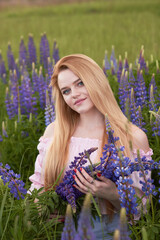 Young attractive long-haired blonde with a bouquet of lupins among a purple field. The concept of nature and romance