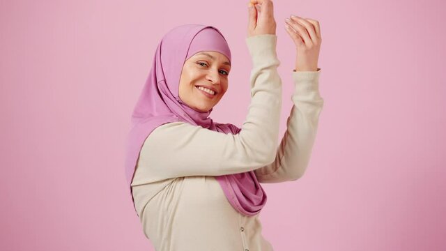 Inspired middle aged muslim woman dancing traditional dance and smiling to camera over pink background