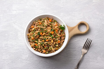 Delicious vegetarian buckwheat with cabbage, carrots, onions, nuts and herbs on a light gray textured background, top view. Homemade diet healthy food