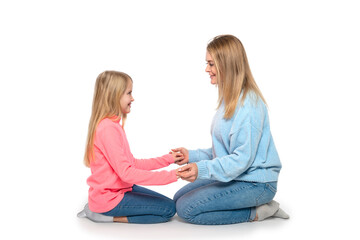 Mom and daughter sit on the floor holding each other's hands with love against white background in studio