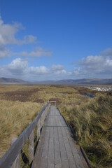 the wooden gangway over the top of the sand dunes at ynyslas beach and nature reserve with a view of the welsh mountains behind it
