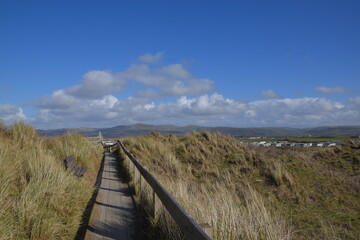 the wooden gangway over the top of the sand dunes at ynyslas beach and nature reserve with a view of the welsh mountains behind it