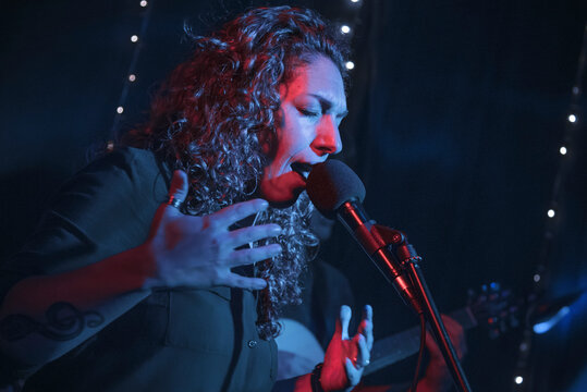 Curly hair woman performing music show with microphone. Rock pop female star singer performer with treble clef tattoo on her arm. Lights music concert
