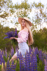 Young attractive blonde in a straw hat with a bouquet of lupins, among a purple field. The concept of nature and romance.