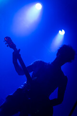 Obraz na płótnie Canvas Unrecognizable male curly hair guitarrist. Music lights show silhouette during rock band live concert. Foggy light
