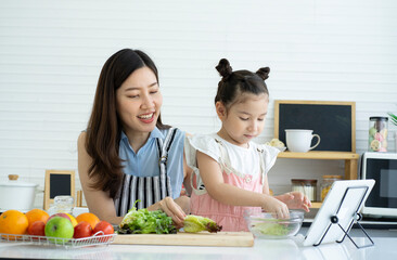 Cute daughter and mom learn to cook with an app to cook healthy and nutritious salads in the kitchen in the evening. 