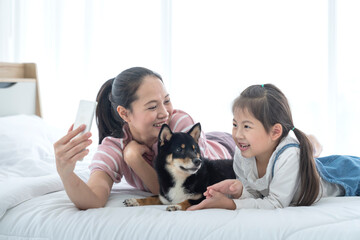 A mother and baby Take a selfie  with a Shiba Inu dog on the bed.