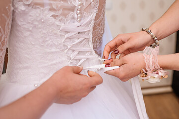 Bridesmaids tie a bow on the wedding dress. Preparing the bride. Morning of the bride