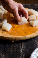 Fototapeta na wymiar Hands of elderly woman who takes a cod fillet with knife on cutting board
