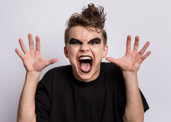 Crazy teen boy with spooking make-up making horns with fingers, isolated on white background. Teenager in style of punk goth dressed in black screaming and shouting. Problems of transitional age
