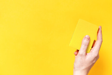 Woman hand holding yellow cleaning sponge on yellow background