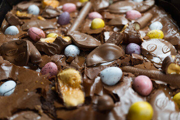 Home baking Easter concept. Brownie with chocolate bars, mini easter eggs and biscuits baked in. Chocolate feast home baked treat
