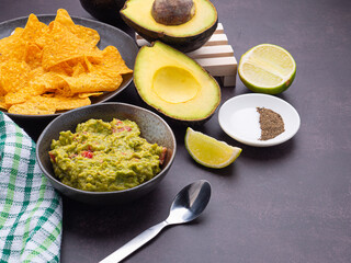 Fresh guacamole on a dish with ingredients for homemade guacamole avocados, lemon, salt, and pepper placed on the old kitchen table. Side view. Concept of traditional Mexican foods