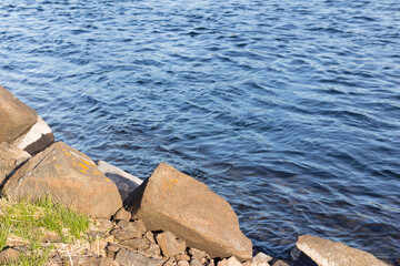 Large rocks, pebbles and grass on the riverbank. The coastline.