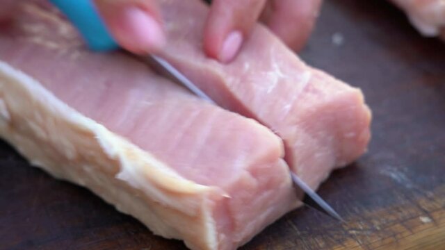 Closeup view 4k stock video footage of woman cutting fresh raw pink pork meat on brown wooden chopping board