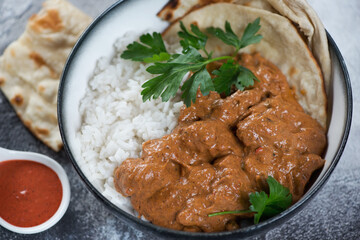 Close-up of a bowl with butter chicken masala, white rice and indian flatbread, selective focus