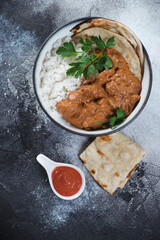 Bowl of indian chicken butter masala over dark grey stone background, vertical shot, view from above