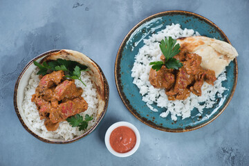 Indian chicken makhani served with rice, flatbread and fresh greens, top view on a grey concrete surface, horizontal shot