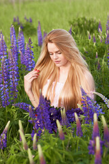 Young attractive long-haired blonde with a bouquet of lupins among a purple field. The concept of nature and romance.