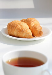 White cup with black tea and croissants in a saucer on the windowsill. Tea ceremony. Sweet morning.