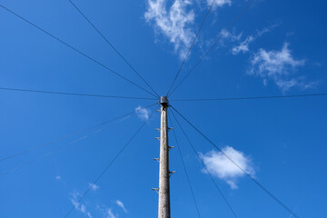 Wooden utility or electrical pole and wires against bright blue sky with white clouds.
