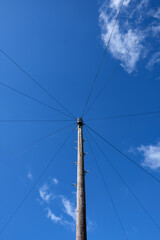 Wooden utility or electrical pole and power lines against bright blue sky with white clouds.