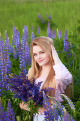 Young attractive long-haired blonde with a bouquet of lupins among a purple field. The concept of nature and romance.