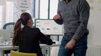 Businessman with face mask touching elbow for greeting his collegue while working at communication project in business office. Coworkers respecting social distancing during coronavirus global pandemic